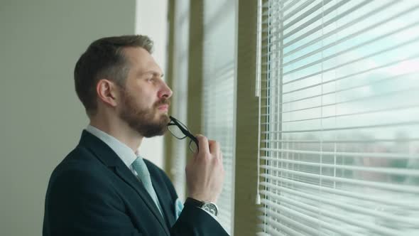 Focused Businessman in a Suit Stands at the Window in the Office and Reflects the Thought Process