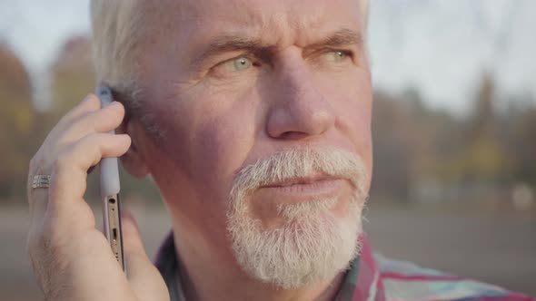 Close-up Portrait of Mature Caucasian Man Standing in the Autumn Park and Talking By Smart Phone