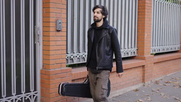 Happy Man Holding a Guitar Case While Walking