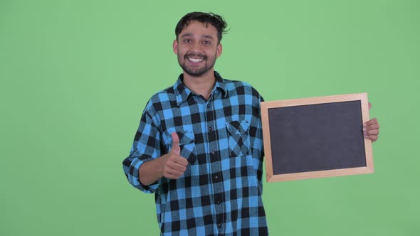 Happy Young Bearded Persian Hipster Man Holding Blackboard and Giving Thumbs Up