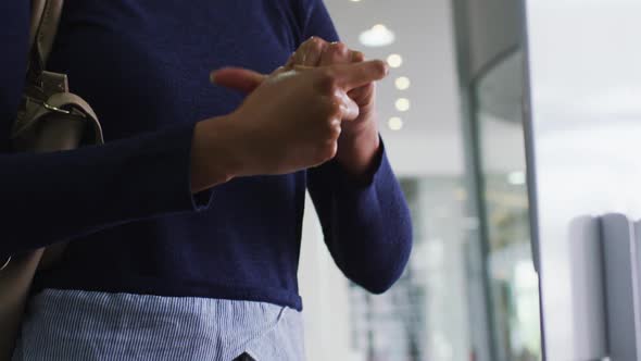 Mixed race businesswoman in face mask disinfecting hands upon arrival in office