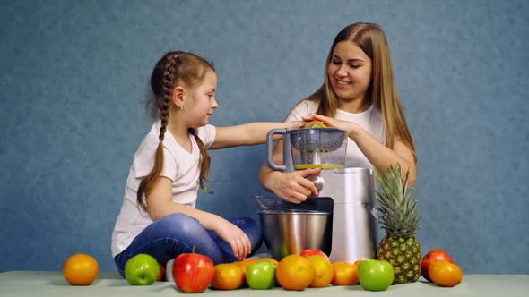 Little girl making fresh juice. Cheerful mother with daughter sitting at table, making fresh juice