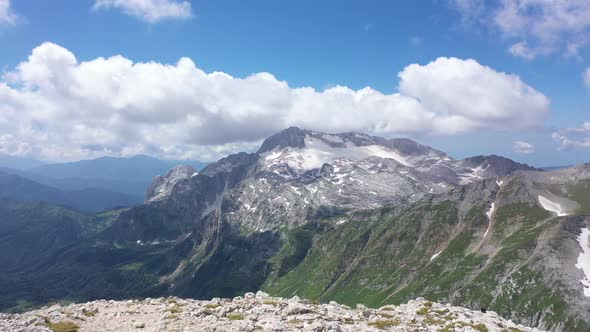 Aerial View of Young Couple on a Mountain Ridge Against Rocky Cliffs, Glacier and Snowy Peaks of