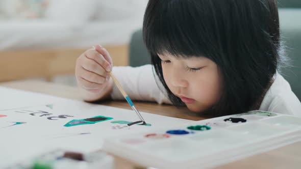 Happy Asian girl drawing picture with water color on paper.