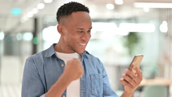 Portrait of Casual African Man Celebrating on Smartphone 