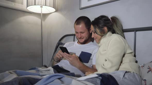 Couple addicted to social media networks spending time in bed together hugging 