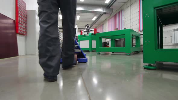 A Man Rolls a Trolley Through an Industrial Warehouse