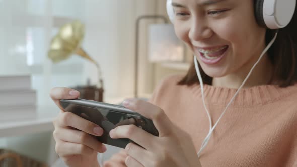 Woman wear white headphone on the head and playing games on smartphone.