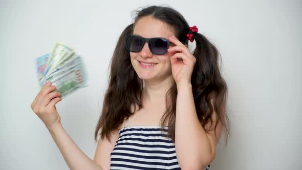 A Young Cheerful Woman in Sunglasses Waves Money Like a Fan