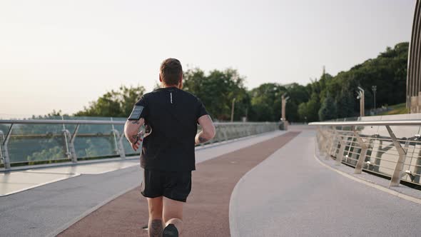 Man Runs on Red Track on Footbridge Near Big Arch in Morning