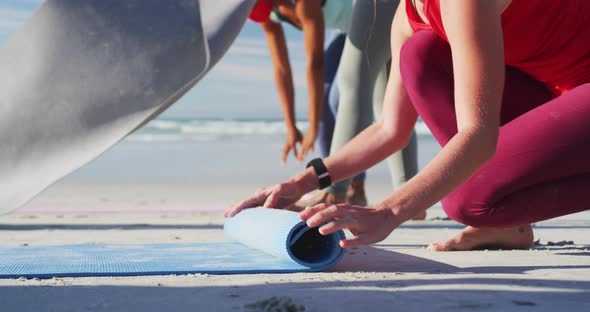 Group of diverse female friends rolling yoga mats after practicing yoga at the beach