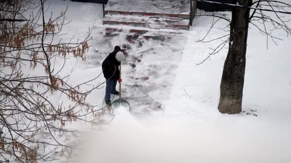 Person Cleans Snow From Sidewalk To House with Large Shovel