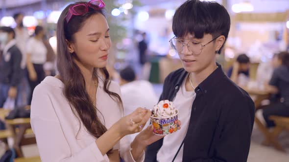 A Beautiful Lady Feed Her Girlfriend an Ice Cream While They're Walking on Street During Their Date