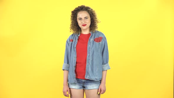 Young Woman Standing, Spreads Out in a Smile and Looks at the Camera on Yellow Background at Studio