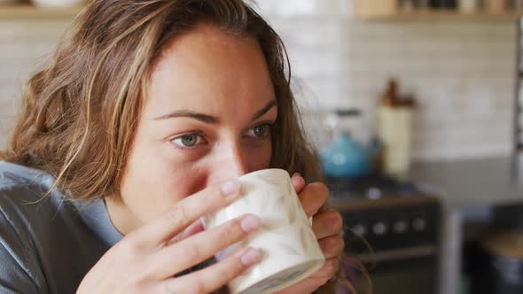 Thoughtful caucasian woman in sunny cottage kitchen drinking coffee