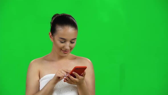 Brunette Girl in a Towel Looks Through Information on the Mobile Phone, Is Surprised and Smiling