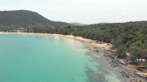 Rocky gold sandy shoreline with lush green hills encircling the shallow turquoise waters, M'pai Bay