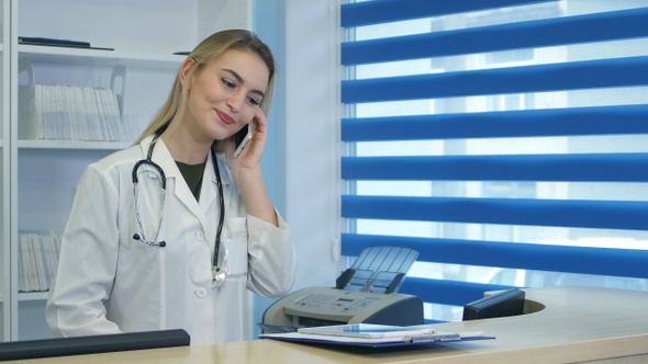 Pretty nurse using tablet and phone at hospital reception desk