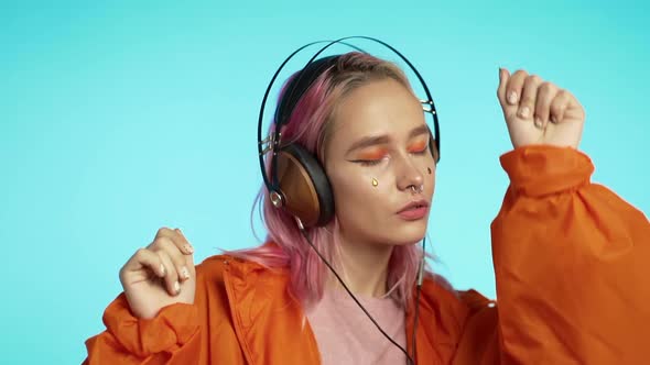 Hipster Woman with Extraordinary Appearance in Headphones in Orange Raincoat on Blue 