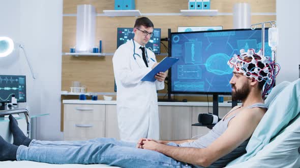 Doctor Analysing Patient Sitting on Bed and Wearing Brain Scanning Device