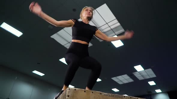 Fit woman jumping on cube in gym