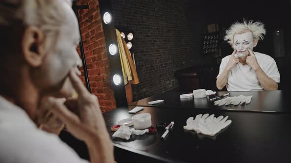 Mime Stretches Facial Muscles at Table Against Mirror