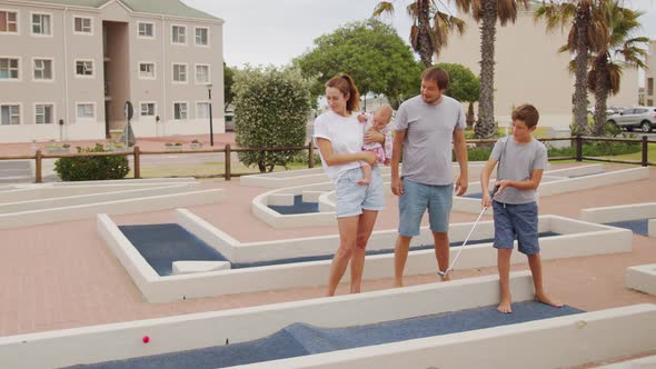 Family of Four Playing on Miniature Golf Course Boy Making Putt Into Hole