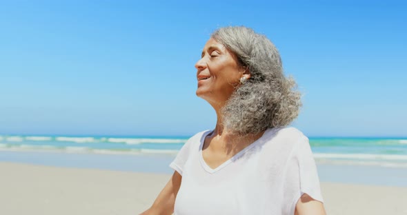 Front view of active senior African American woman with arms stretched out standing on beach 4k