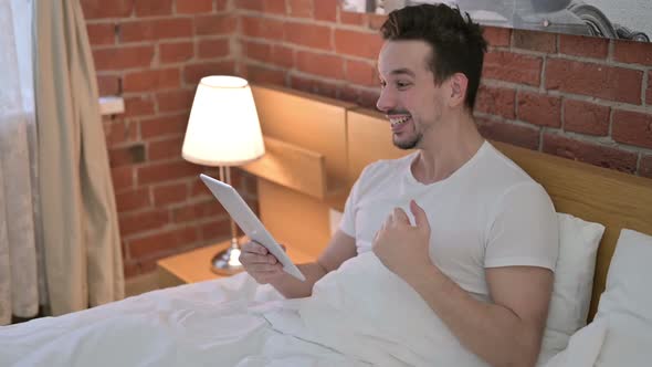 Young Man Celebrating Success on Tablet in Bed