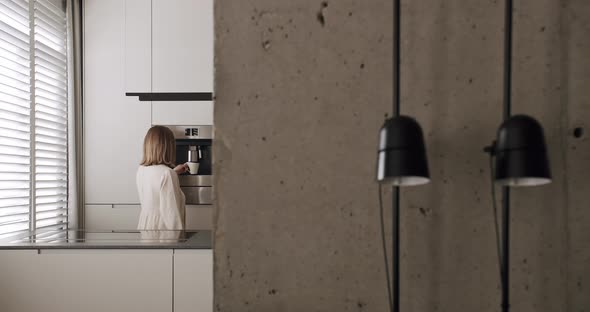 A Woman Makes a Coffee in a Minimalist Interior with Focus on the Lamp