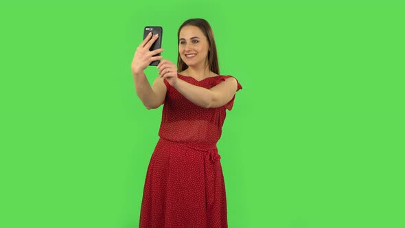 Tender Girl in Red Dress Is Making Selfie on Mobile Phone Then Looking Photos. Green Screen