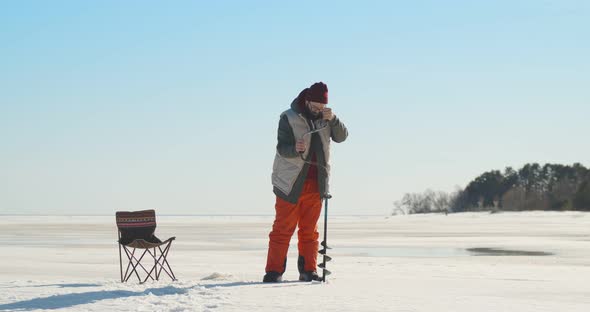Young Fisherman Making Hole with Drill for Ice Fishing