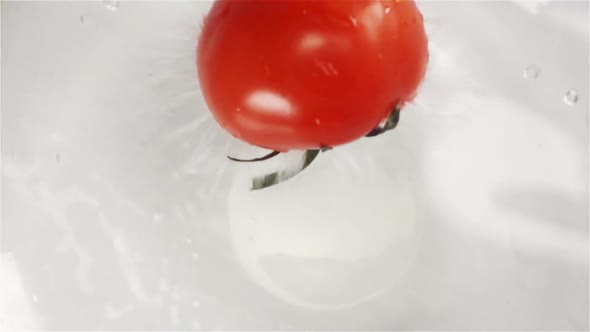 Red Tasty Fresh Tomato with Green Leaves Falls Under Water with Splash and Spray