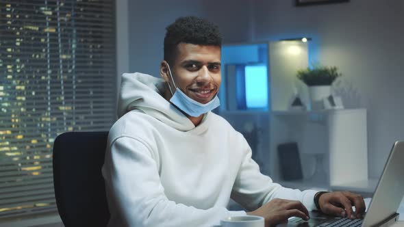 Medium Shot of Handsome Black Man with Medical Mask Smiling To the Camera While Working Home