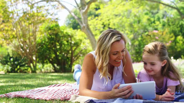 Happy mother and daughter using digital tablet in park 4k