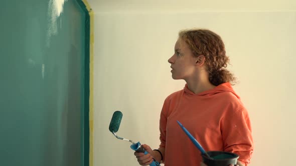 Beautiful Young Girl Paints the Wall Blue While Standing on a Stepladder
