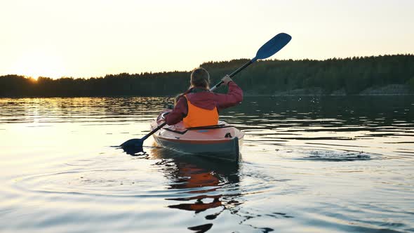 Mother in Vest Rows Sports Kayak with Girl Along River