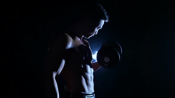 Athlete Is Training His Muscles with a Dumbbell, Black Background, Slow Motion, Silhouette