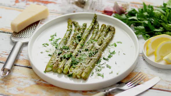 Delicious Roasted Asparagus Served on White Ceramic Plate. With Parmesan Cheese, Parsley and Lemon.