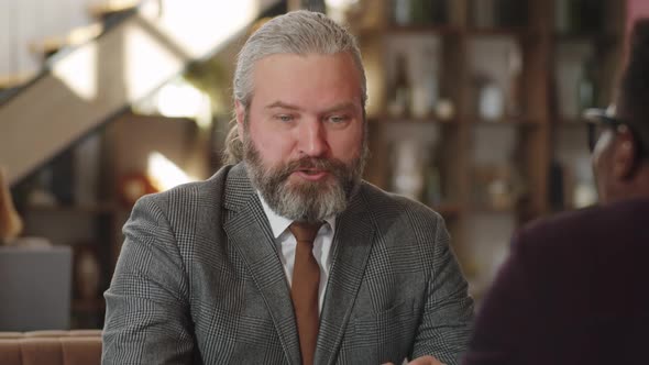 Senior Businessman Shaking Hands and Talking with Colleague in Cafe