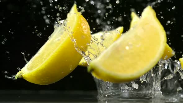 Slo-motion lemon falling into wedges against black drop