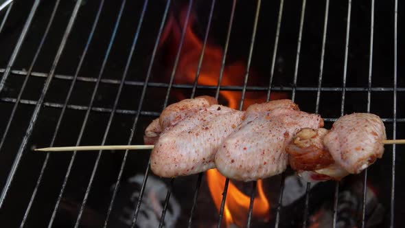 Raw Chicken Wings on Wooden Skewers are Placed Above the Open Fire on the Grill