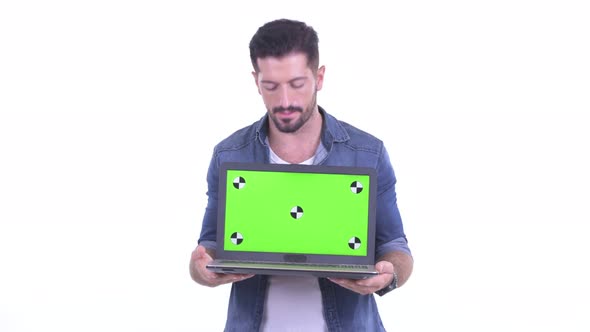 Happy Young Bearded Hipster Man Talking While Showing Laptop