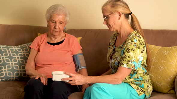 Home healthcare nurse and elderly woman taking blood pressure with a machine.