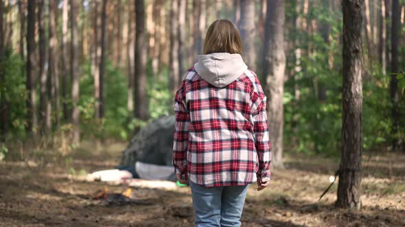 Tracking Shot of Happy Woman Walking to Burning Fire Sitting Down at Tent in Forest