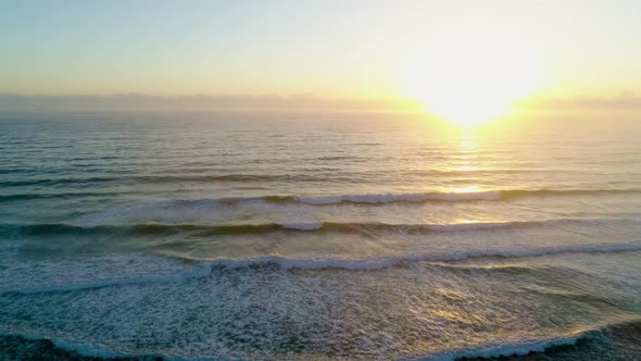 Static aerial view of crushing waves facing the sun at sunset