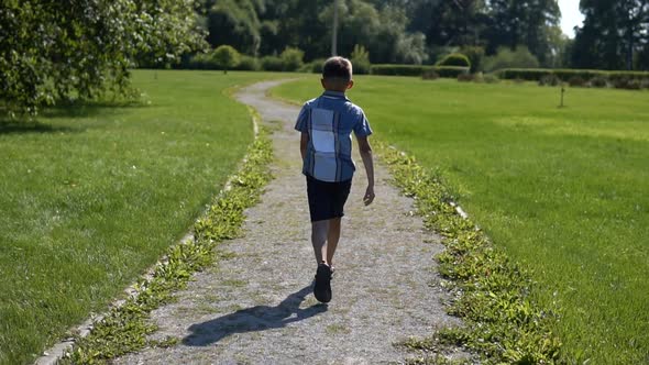 the Boy Runs Along the Grass in the Park Having a Good Mood in Sunny Weather