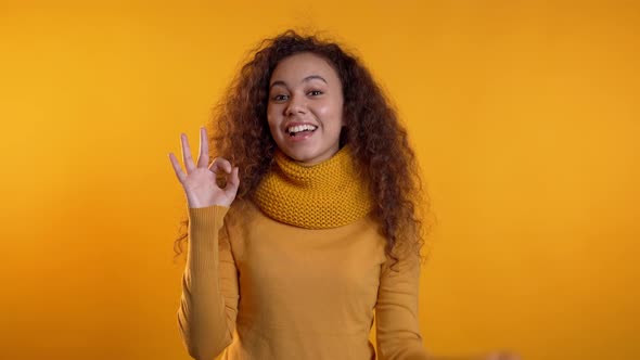 Positive Girl Making OK Sign Over Yellow Background and Smiles To Camera