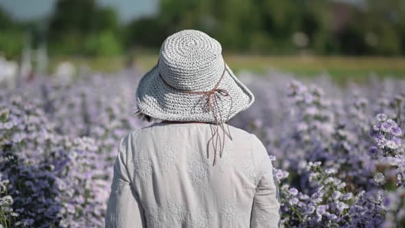 Asian woman walking in a flower garden and looking back at the camera, slow motion.