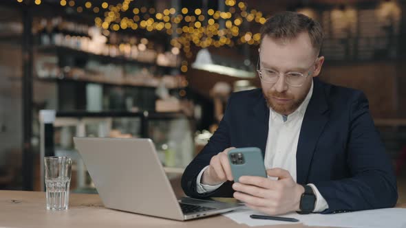 Businessman Using Smartphone at the Cafe While Texting Messages to Clients